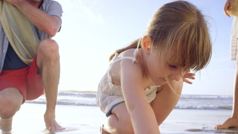 Glückliche-Familie,-Die-Am-Strand-Spielt-Mädchen,-Das-Bei-Sonnenuntergang-Im-Sand-Zeichnet