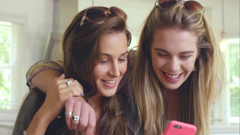 Two-beautiful-friends-planning-road-trip-using-smart-phone-at-home