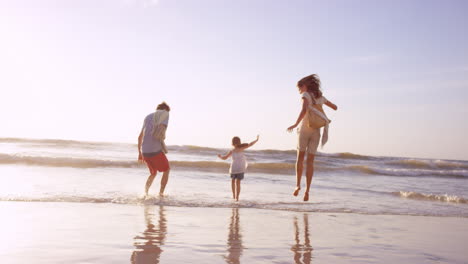 Familia-Feliz-Jugando-En-Las-Olas-En-La-Playa-Al-Atardecer-De-Vacaciones