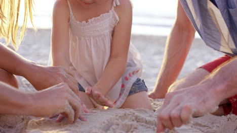 Glückliche-Familie,-Die-Am-Strand-Spielt-Und-Bei-Sonnenuntergang-Im-Sand-Zeichnet