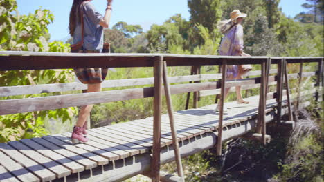 Two-beautiful-friends-on-adventure-trail-wooden-bridge-looking-at-nature