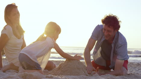 Glückliche-Familie,-Die-Am-Strand-Spielt-Und-Bei-Sonnenuntergang-Eine-Sandburg-Baut