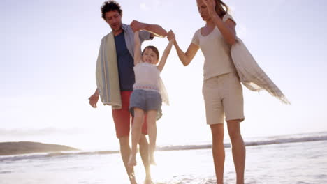Happy-family-on-the-beach-holding-hands-swinging-little-girl-around-at-sunset-on-vacation