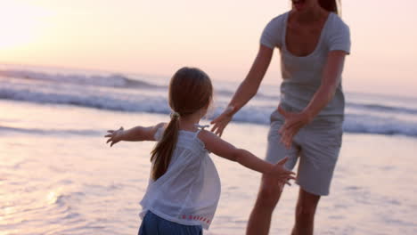 Mutter-Schwingt-Kleines-Mädchen-Um-Glückliche-Familie-Am-Strand-Und-Hält-Händchen-Bei-Sonnenuntergang-Im-Urlaub