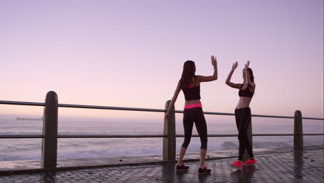 Two-athletic-friends-stretching-before-a-run-on-promenade-at-sunset