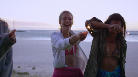 Teenage-girls-celebrating-and-laughing-with-bright-sparklers-dancing-in-slow-motion-on-beach