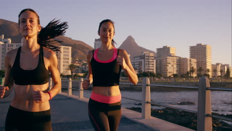 Two-athletic-woman-running-outdoors-slow-motion-on-promenade-at-sunset-near-ocean-enjoying-evening-run