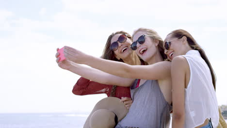 Group-of-teenage-girls-taking-selfie-using-smartphone-on-vacation-outdoors-beach-promenade
