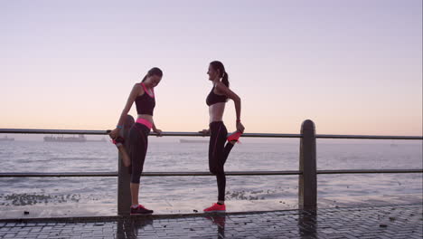 Two-athletic-friends-stretching-before-a-run-on-promenade-at-sunset