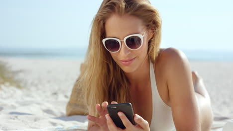 Schöne-Frau,-Die-Ein-Telefon-SMS-Gespräch-Benutzt-Und-Am-Strand-Liegt-Und-Sich-Bräunt