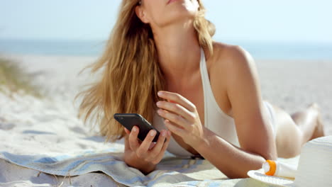 Hermosa-Mujer-Usando-Conversación-De-Mensajes-De-Texto-Telefónico-Tumbado-En-La-Playa-Bronceándose