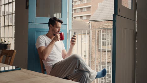 Morning-coffee-for-happy-man-using-smart-phone-at-home-in-pajamas