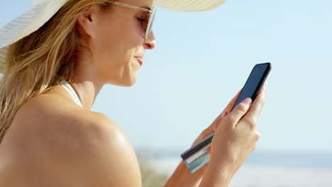 Mujer-Usando-Tarjeta-De-Crédito-Comprando-En-Línea-Con-Teléfono-Móvil-En-La-Playa-De-Vacaciones
