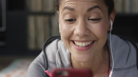 Close-up-of-happy-mixed-race-woman-talking-to-her-friend-online-using-smart-phone-app-with-earphones-at-home
