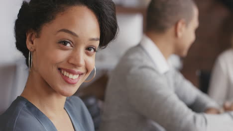Portrait-of-a-confident-young-hispanic-business-woman-at-boardroom-table-in-office-space-a-diverse-team-in-background-In-slow-motion-turning-around-smiling