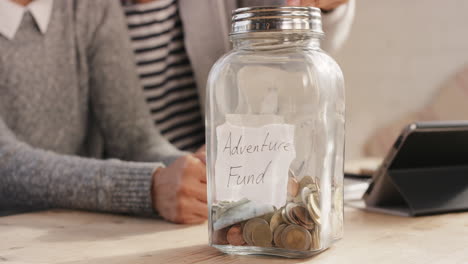 Glückliches-Gemischtrassiges-Paar,-Das-Geld-Im-Abenteuerfonds-Glas-Spart