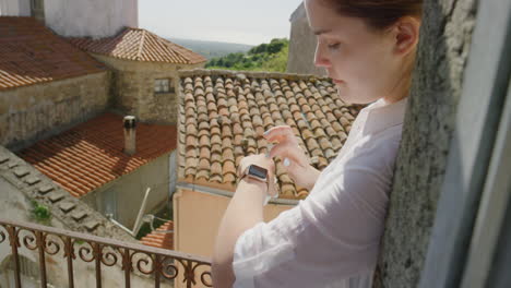Mujer-Usando-Reloj-Inteligente-Revisando-Mensajes-Bebiendo-Café-Disfrutando-De-Un-Cálido-Día-Soleado-De-Vacaciones-De-Pie-En-El-Balcón-Turista-Feliz-Relajándose-En-Italia