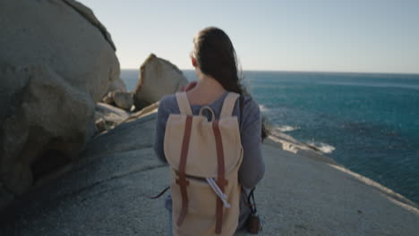close-up-of-young-brave-woman-walking-on-beautiful-ocean-seaside-enjoying-adventure-exploring-independent-vacation-lifestyle-wearing-backpack