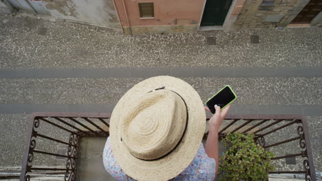 Frau-Nutzt-Smartphone,-Trinkt-Kaffee-Und-Genießt-Den-Sommerurlaub,-Stöbert-In-Online-Nachrichten,-Entspannt-Auf-Dem-Balkon-Und-Schreibt-SMS-Mit-Hut-Von-Oben