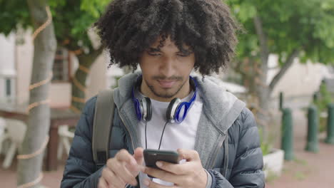 portrait-of-young-male-mixed-race-student--texting-browsing-online-using-smartphone-social-media-in-urban-city-background