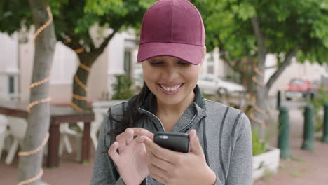 portrait-of-young-attractive-mixed-race-woman-smiling-enjoying-texting-browsing-using-smartphone-wearing-hat-urban-city-background