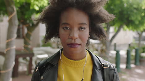 portrait-of-cool-trendy-african-american-woman-student-with-funky-afro-looking-serious-at-camera-listening-to-music-wearing-earphones
