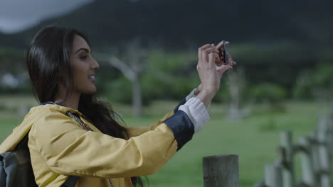 attractive-young-indian-woman-taking-photo-using-smartphone-camera-technology-enjoying-sharing-adventure-travel-hiker-photographing-green-countryside-outdoors-on-mobile-phone