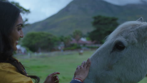 young-indian-woman-petting-horse-smiling-enjoying-bonding-caring-for-equine-pet-friend-showing-affection-in-beautiful-countryside-farm