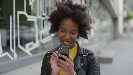 Retrato-De-Una-Elegante-Mujer-Afroamericana-Que-Usa-Mensajes-De-Texto-Con-Un-Teléfono-Inteligente-Navegando-En-Las-Redes-Sociales-En-Línea-Sonriendo-Disfrutando-Leyendo-Mensajes-SMS-En-La-Tecnología-De-Telefonía-Móvil-En-La-Calle-De-La-Ciudad