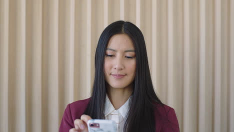 Retrato-De-Una-Joven-Y-Hermosa-Mujer-Asiática-Estudiante-Pasante-Enviando-Mensajes-De-Texto-Navegando-En-Línea-Usando-Tecnología-Móvil-De-Teléfono-Inteligente-Que-Parece-Enfocada-Y-Pensativa
