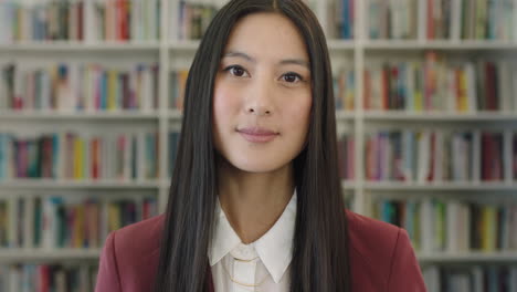 Porträt-Einer-Süßen-Jungen-Asiatischen-Studentin,-Die-Im-Bücherregal-Der-öffentlichen-Bibliothek-Nachdenklich-Und-Ruhig-In-Die-Kamera-Blickt