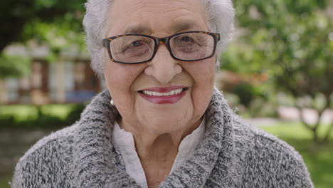 Porträt-Einer-älteren-Rentnerin-Im-Park,-Die-Glücklich-Lächelt-Und-Mit-Brille-In-Die-Kamera-Blickt