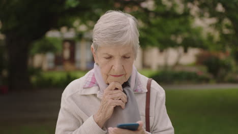 Retrato-De-Una-Anciana-Caucásica-Pensativa-Enviando-Mensajes-De-Texto-Navegando-Usando-Un-Teléfono-Inteligente-En-El-Parque