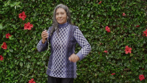 Retrato-De-Una-Hermosa-Anciana-India-Bailando-Juguetona-Disfrutando-Escuchando-Música-Con-Auriculares-En-El-Fondo-Del-Jardín-Al-Aire-Libre-Feliz-Jubilación