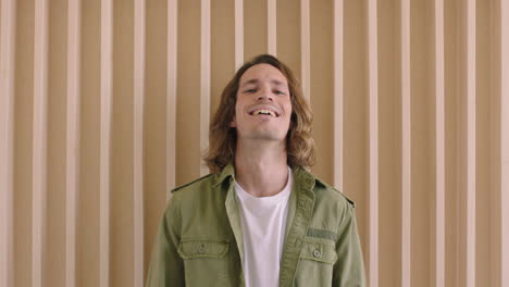 portrait-of-handsome-young-caucasian-man-laughing-cheerful-confident-looking-at-camera-relaxed-male-with-long-hair-wooden-backgroud