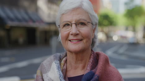 portrait-of-friendly-elderly-woman-smiling-looking-at-camera-wearing-scarf-in-city-street-background-slow-motion
