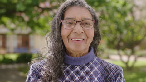Porträt-Einer-Hübschen-älteren-Indischen-Frau,-Die-Glücklich-Lächelt-Und-Im-Gartenhintergrund-In-Die-Kamera-Blickt