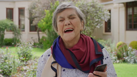 Porträt-Einer-Glücklichen-älteren-Frau,-Die-Ihr-Smartphone-Benutzt,-Fröhlich-Lacht-Und-Es-Genießt,-Online-Medien-Mit-Dem-Mobiltelefon-Im-Garten-Ihres-Altersheims-Anzusehen