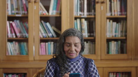 Porträt-Einer-älteren-Indischen-Frau-In-Der-Bibliothek,-Die-Mit-Der-Smartphone-Messaging-App-SMS-Schreibt-Und-Glücklich-Lächelt
