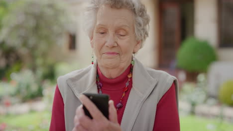 Porträt-Einer-Glücklichen-älteren-Frau,-Die-Ihr-Smartphone-Nutzt,-Um-SMS-Zu-Schreiben-Und-Zu-Surfen-Und-Messaging-SMS-über-Die-Mobiltelefon-Technologie-App-Im-Sonnigen-Hintergrund-Des-Altersheimgartens-Zu-Senden