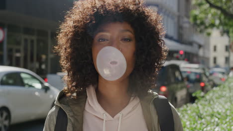 portrait-of-young-african-american-woman-blowing-bubblegum-smiling-happy-enjoying-playful-fun-in-vibrant-urban-city-street-morning-female-student-with-afro-hairstyle