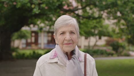 Porträt-Einer-älteren-Kaukasischen-Frau-Im-Park,-Die-Mit-Einem-Schal-In-Die-Kamera-Blickt