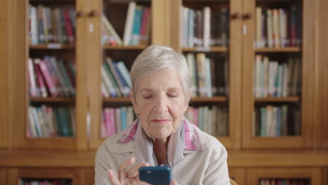 Porträt-Einer-älteren-Kaukasischen-Frau-In-Der-Bibliothek,-Die-Mit-Der-Smartphone-Messaging-App-SMS-Schreibt-Und-Glücklich-Lächelt