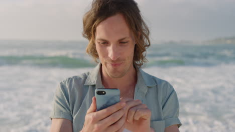 Porträt-Eines-Glücklichen-Jungen-Mannes,-Der-Sein-Smartphone-Nutzt,-Um-SMS-Zu-Schreiben-Und-Online-Zu-Surfen,-Urlaubserlebnisse-In-Sozialen-Medien-Zu-Teilen-Und-Mobile-Kommunikation-Vor-Sonnigem-Strandhintergrund-Zu-Genießen
