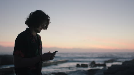 Un-Joven-Usando-Mensajes-De-Texto-Por-Teléfono-Junto-Al-Mar-Esperando-El-Amanecer