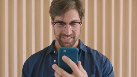 slow-motion-portrait-of-attractive-young-hipster-man-wearing-glasses-texting-browsing-enjoying-using-smartphone-mobile-technology-smiling-happy-caucasian-male