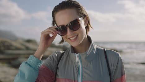 portrait-of-attractive-young-woman-smiling-at-beach-removes-sunglasses