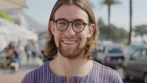 portrait-of-cute-young-man-nerd-wearing-glasses-smiling-enjoying-summer-vacation-sunny-outdoors-looking-calm-on-busy-urban-beachfront-real-people-series