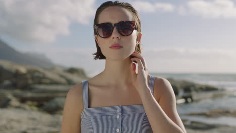 Porträt-Einer-Attraktiven-Frau-Mit-Sonnenbrille,-Die-Ernst-Aussieht-Und-Am-Strand-Haare-Berührt