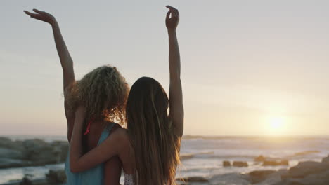 girlfriends-on-beach-looking-at-sunset-embracing-with-arms-raised